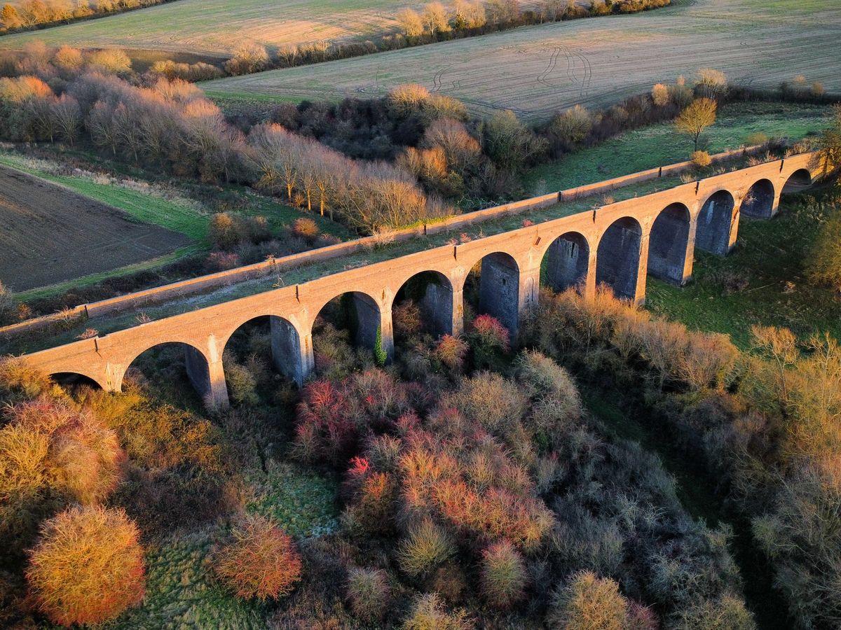 Aerial view of a historic stone railway viaduct across fields